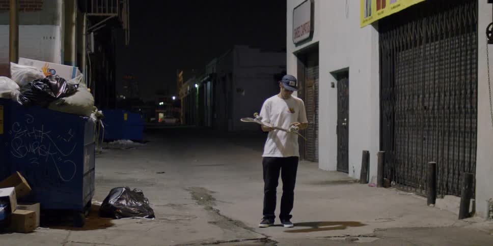 A man is grabs his skateboard in the alley
