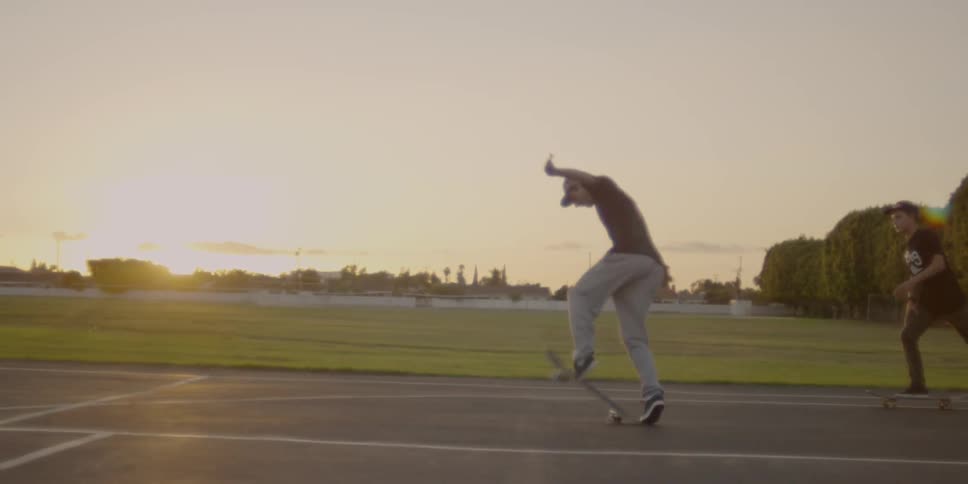 A boy does a trick on a skateboard on a basketball court at sunset