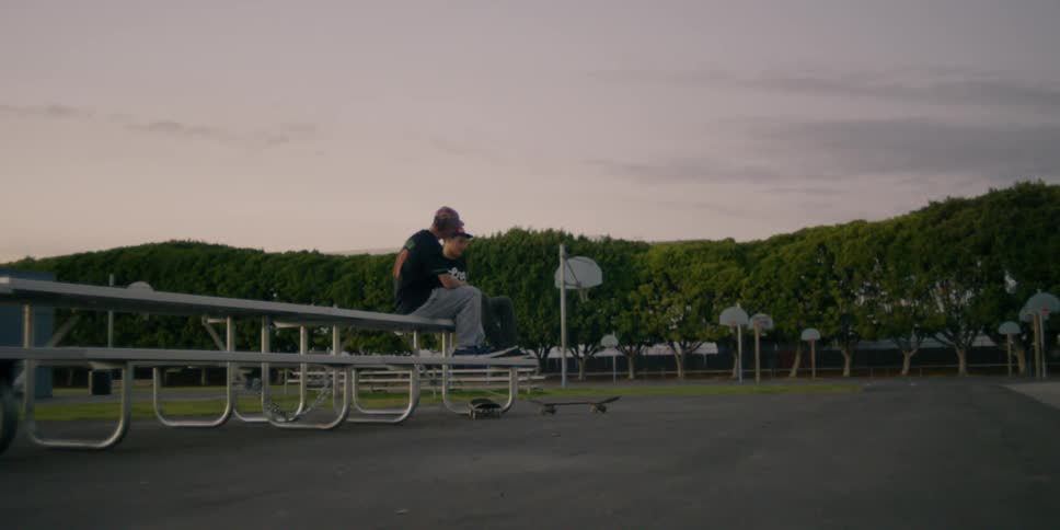 Two people sit on the table by the field and talk