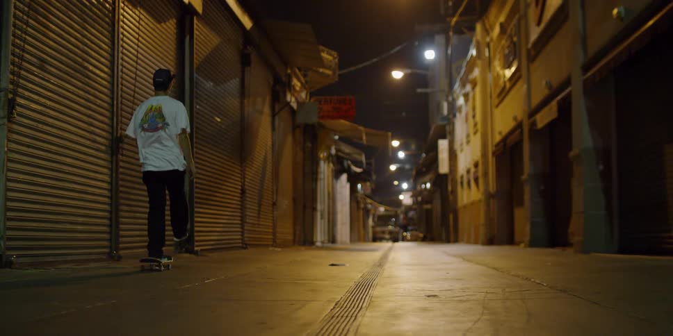 A teenager is riding a skateboard in a city alley at night