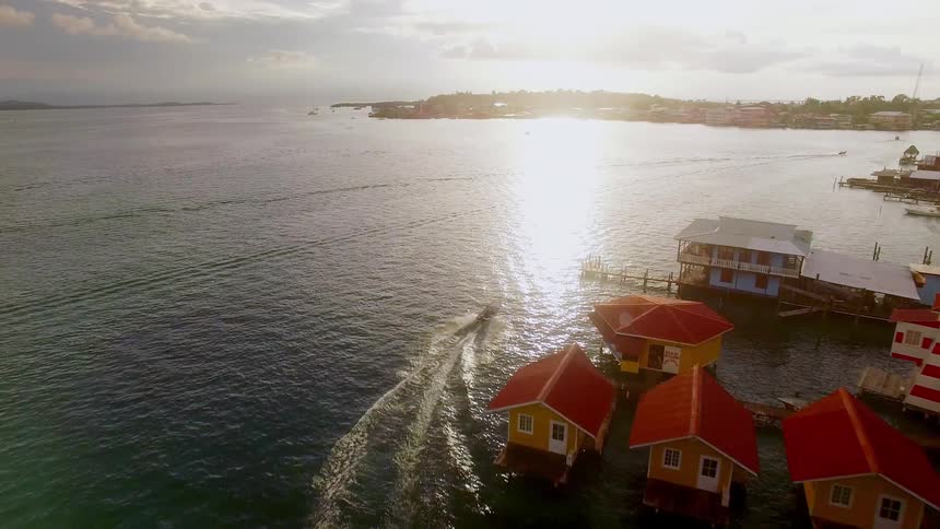 A boat sails around stilt houses floating in the ocean in a tranquil vacation town in Panama