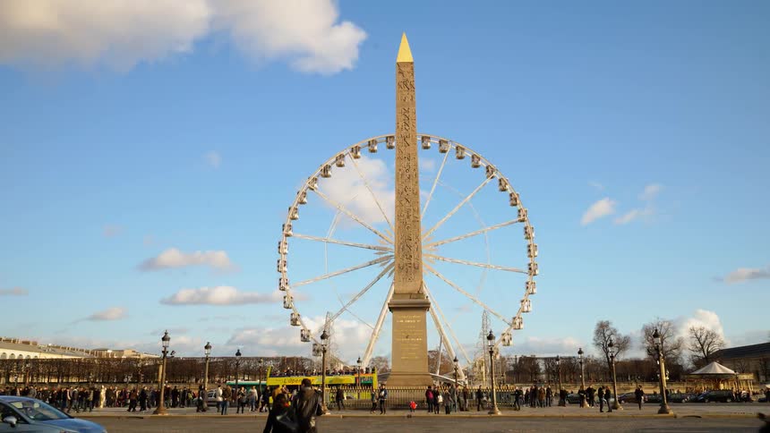 A giant ferris wheel is spinning near an obelisk as they day passes