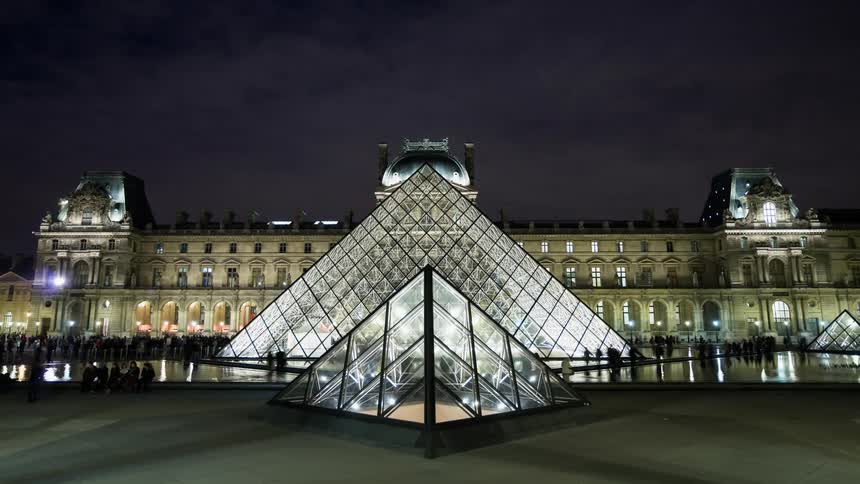 People pass by and mill about the louvre museum at night