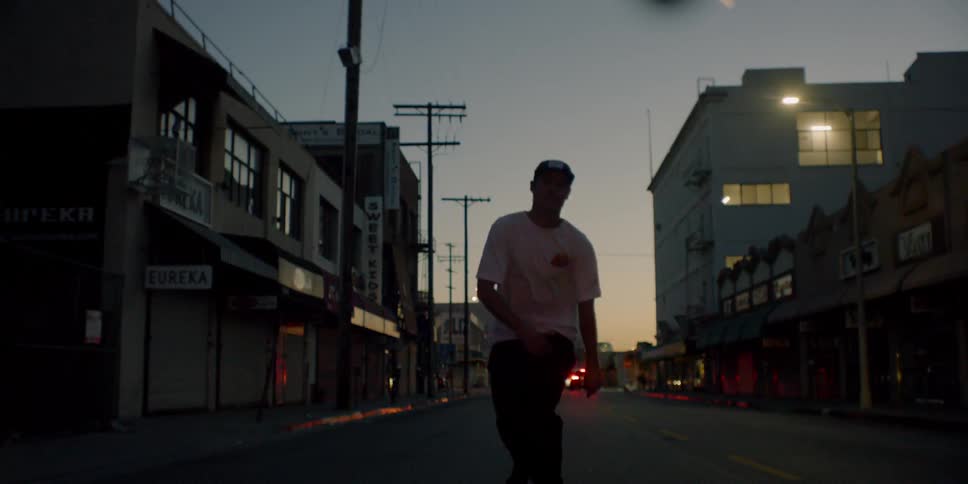 A teenager is riding a skateboard on a city street at dusk