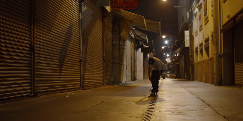 A teenager is riding a skateboard in a city alley at night