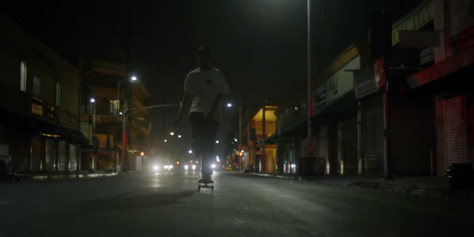 A teenager is riding a skateboard on a city street at night