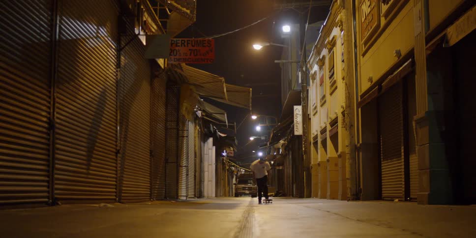 A teenager is riding a skateboard in a city alley at night