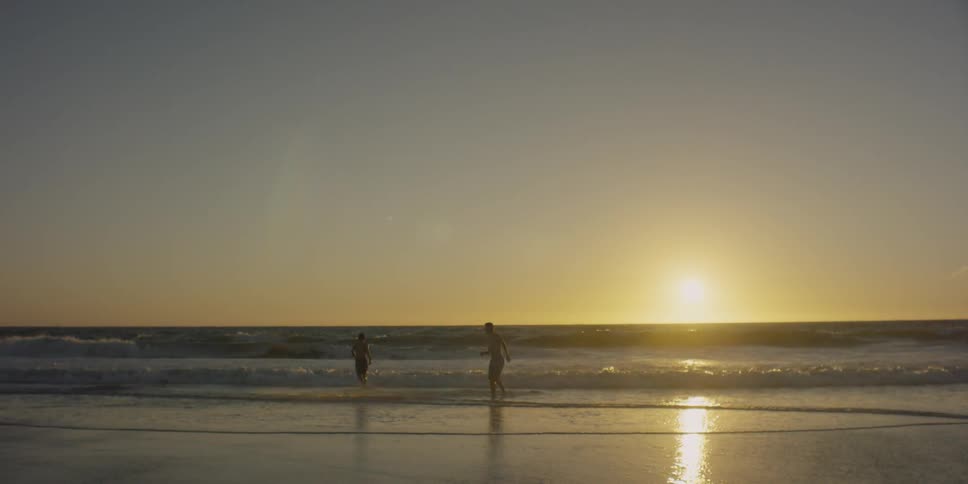Two people play in the waves on the beach at sunset