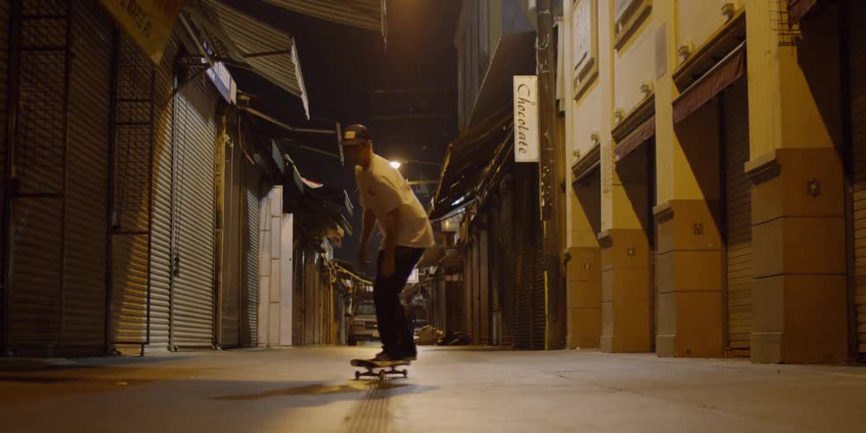 A man rides his skateboard back and forth and jumps in the alley