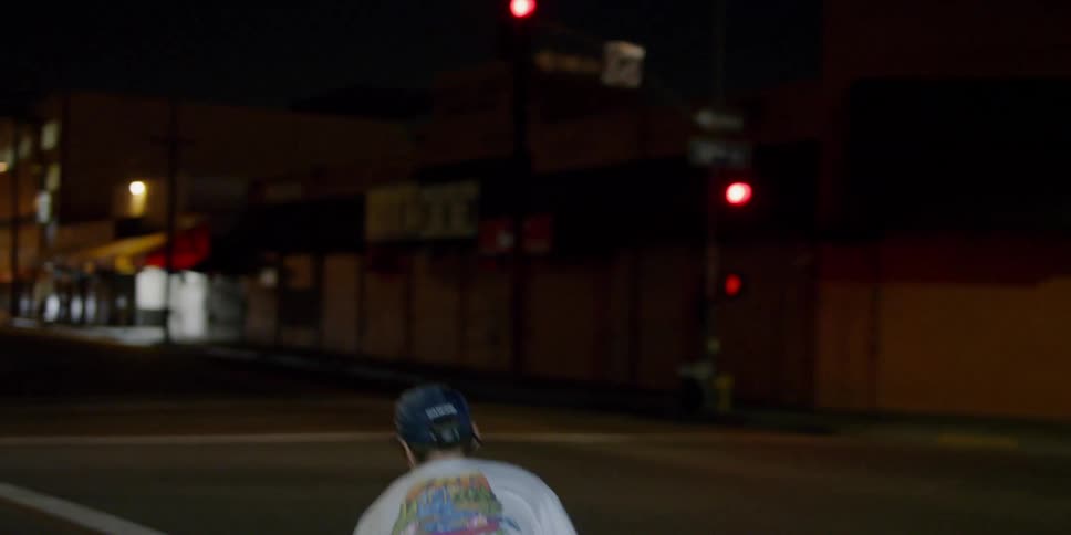 A teenager is riding a skateboard across a crosswalk at night