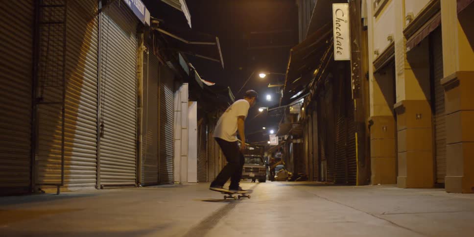 A man rides his skateboard towards a car in the alley