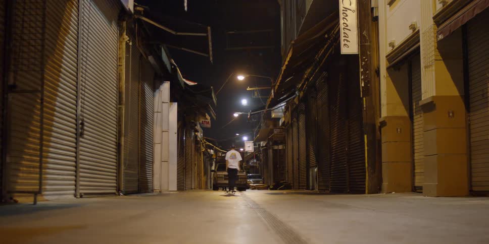 A skateboarder rides down a city alley at night