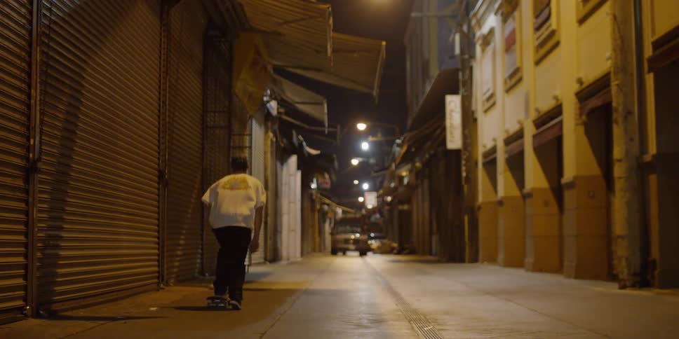 A teenager is skateboarding in an alley at night