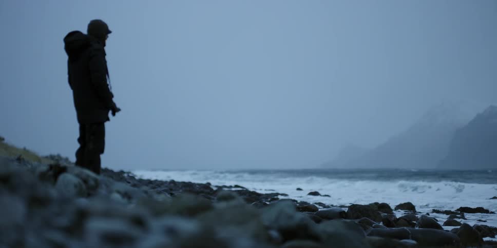 A man stands on the rock covered shore