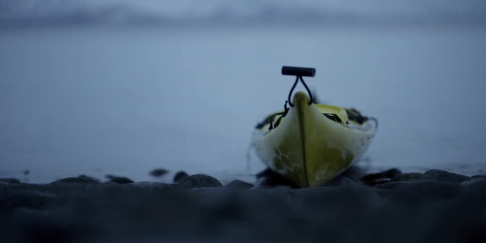 A kayak sits on the rocky shore