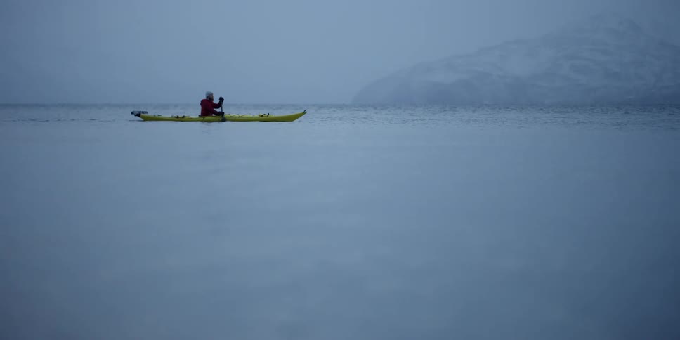 A man paddles a kayak on cold waters as it snows