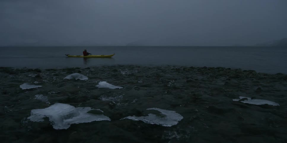 A man paddles a kayak in the icy sea