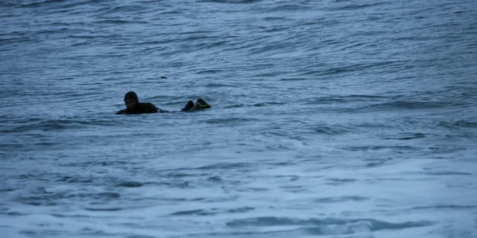 A surfer in a wet suit paddles through the waves