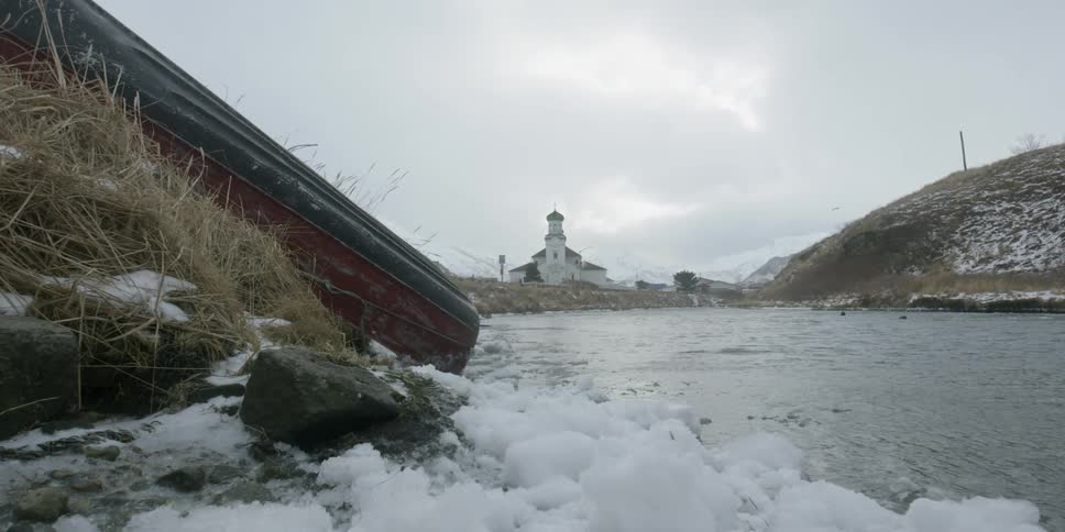 Water flowing in a river with snow on the banks with a building on shore