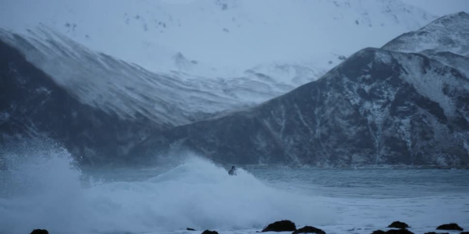 A surfer rides a wave towards the shore in winter