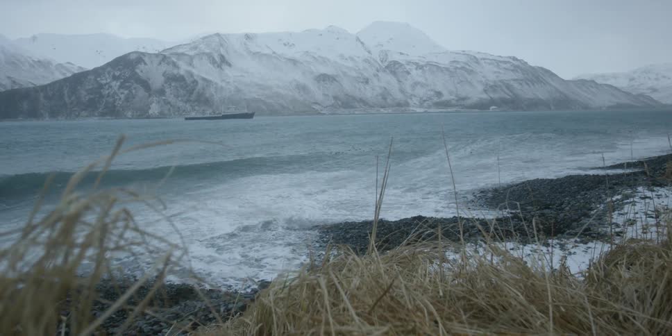 A boat travels on the water in front of a snow covered mountain