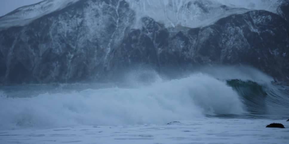 A wave crashes over a surfer in winter