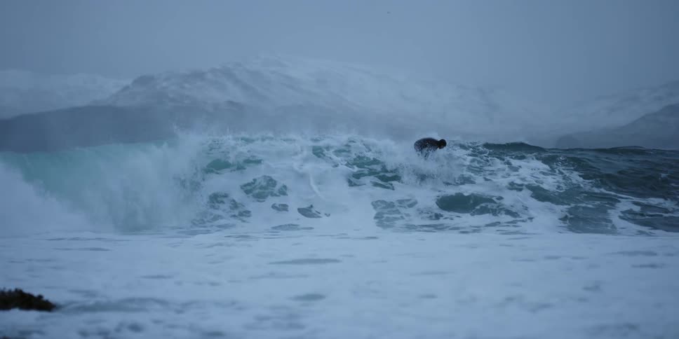 A surfer rides a wave on a snowy day