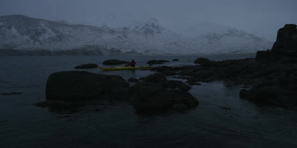 A person paddles a kayak in winter