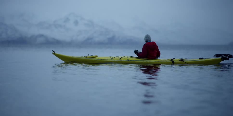A man paddles a kayak on the sea as it snows