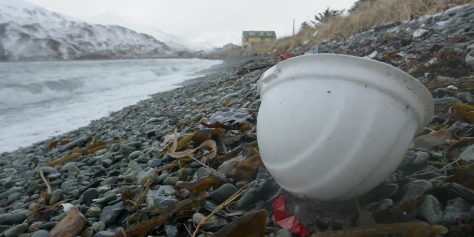 A hardhat and other debris sit on a rocky shore