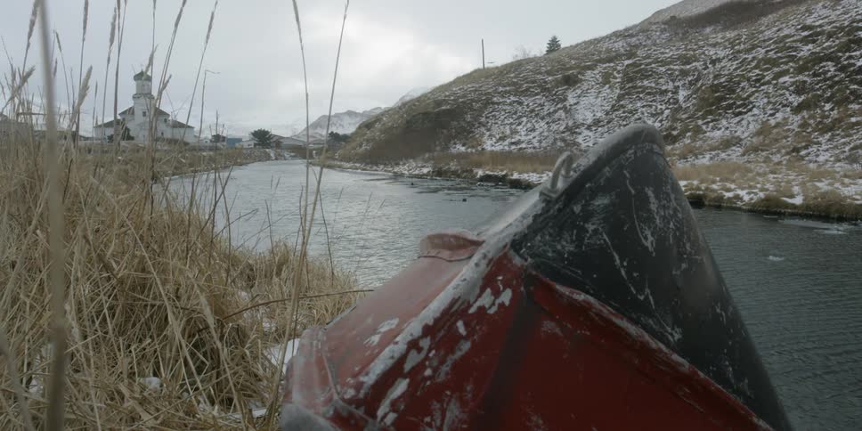 Water flowing in a stream surrounded by hills and an abandoned fishing boat on shore