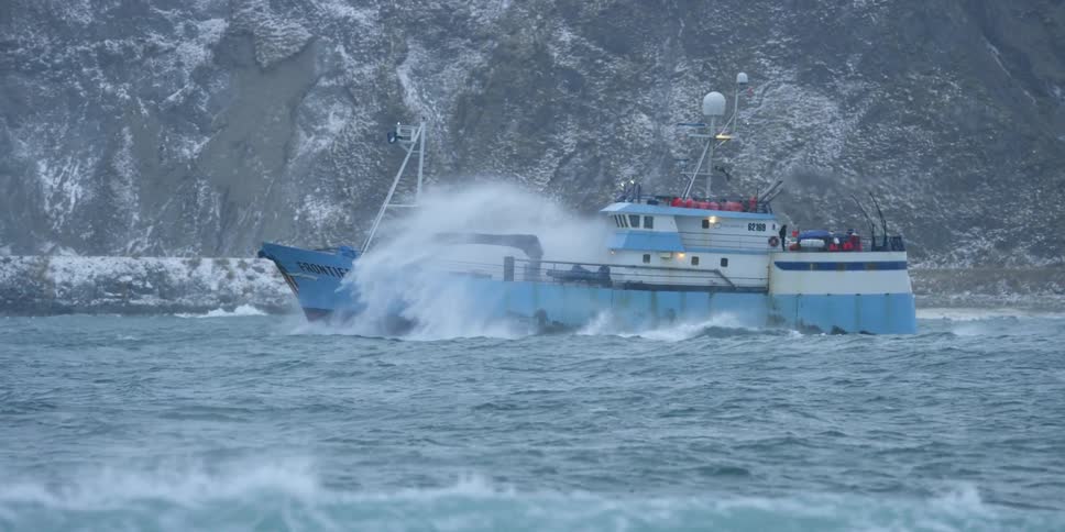 A fishing boat crashes through ocean spray