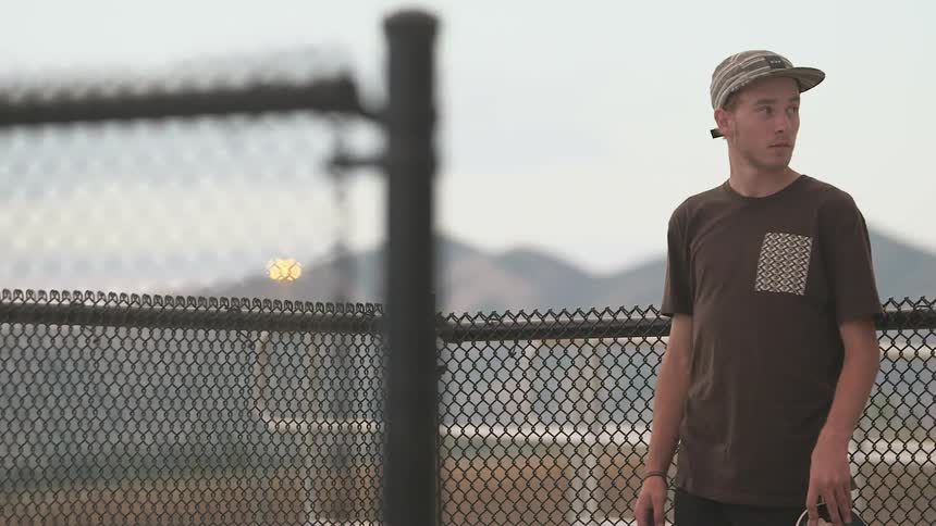 A guy stands by a fence holding a skateboard