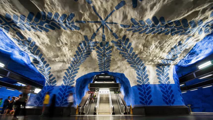 Commuters walk in a subway station with decorated walls and ceiling