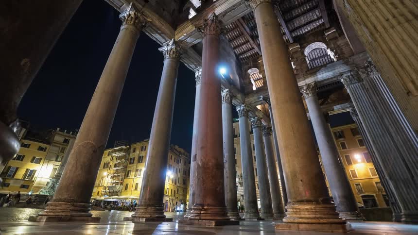 Pedestrians walk by a building with pillars