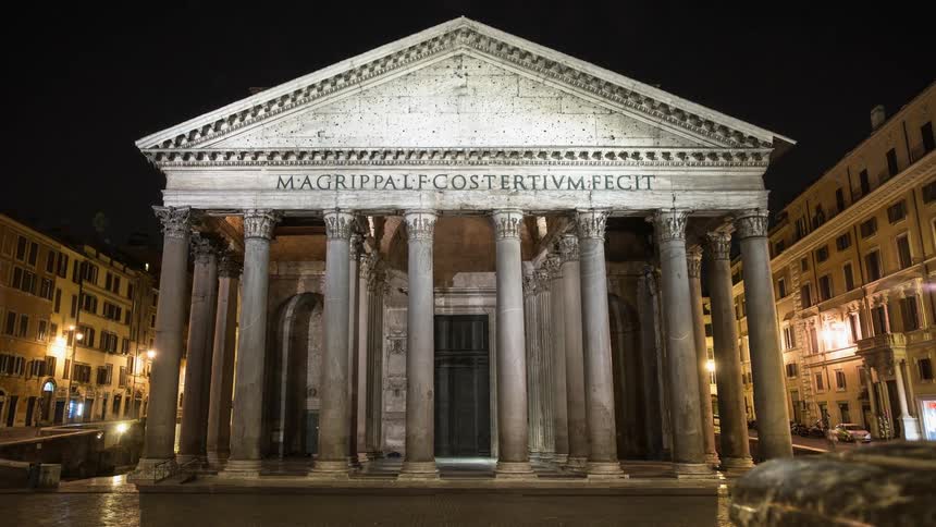 A stone building with pillars stands in a city at night