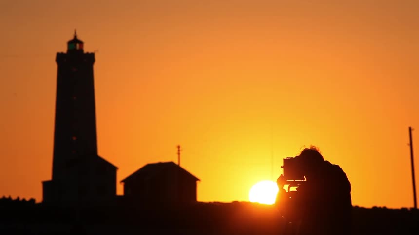 A photographer sets up a photo of a lighthouse at sunset