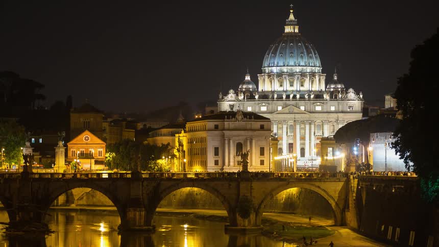 People walking over a bridge near a cathedral at night