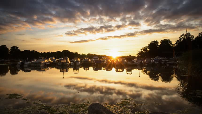 Clouds pass over a still lake with boats parked on it