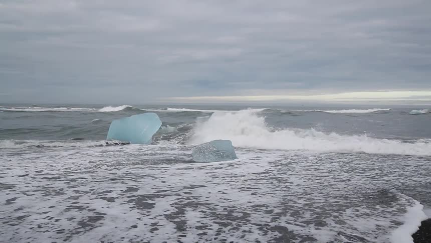 Ocean waves crash over ice on a shore