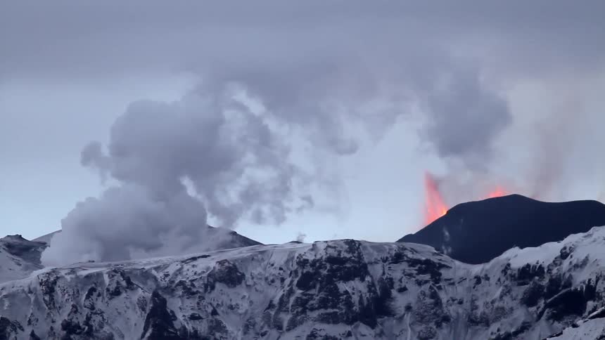 Lava shoots up from a volcano near snowy mountains