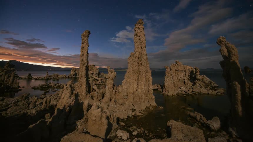 Clouds pass over rock formations on the shore as the sun sets
