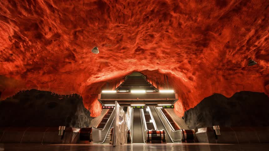 People going up and down an escalator into a red-walled subway station