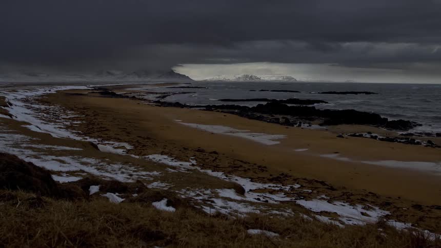 Clouds move over the ocean and beach with snow