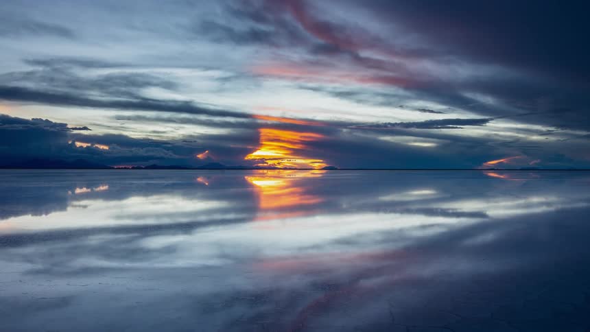 Clouds and sun light are reflected on the water as the sunsets