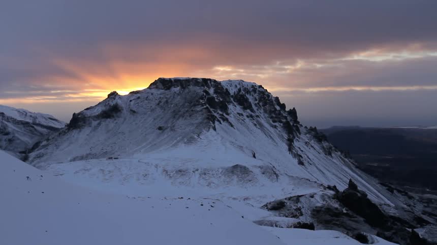 Sun setting behind snowy mountains on a cloudy evening