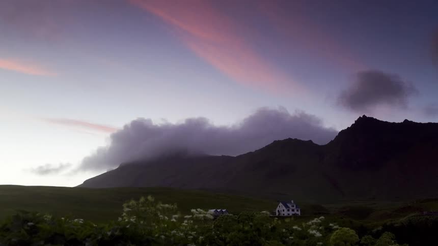 A white building sits on a grassy slope as clouds move over hilltops