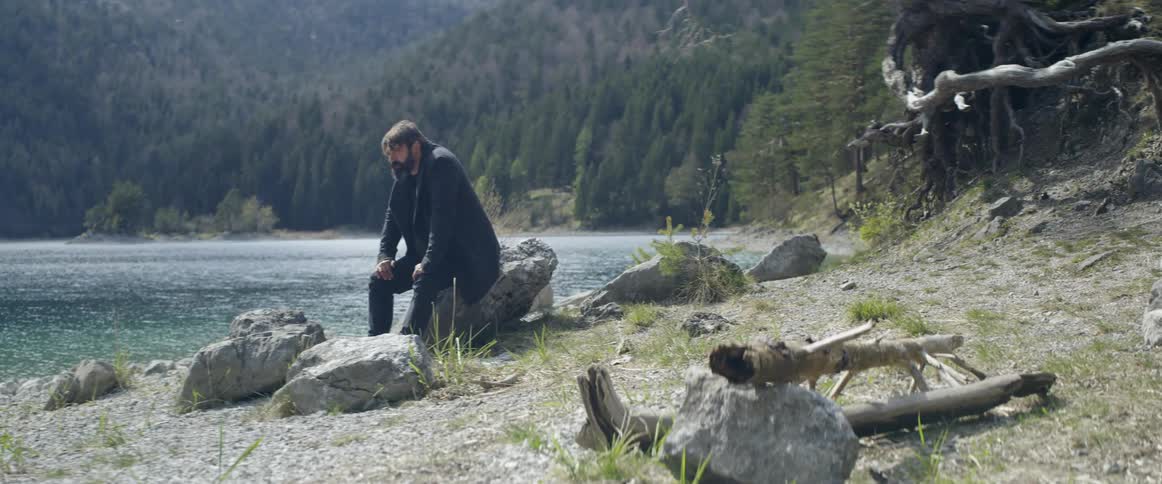 A man sits on a rock next to the water