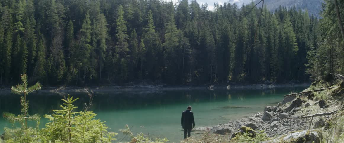 A man stands on the edge of a river in the forest
