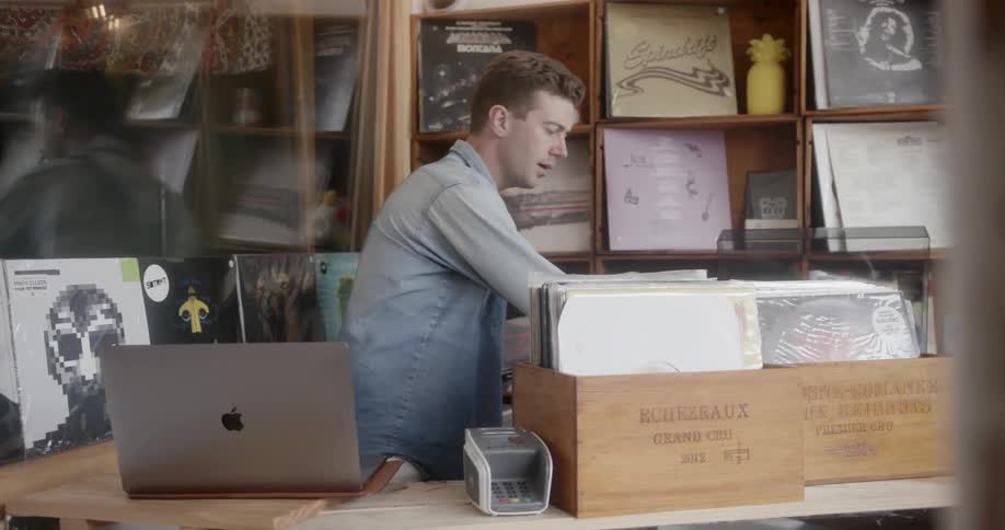 A record store worker writes in a notebook and organizes albums